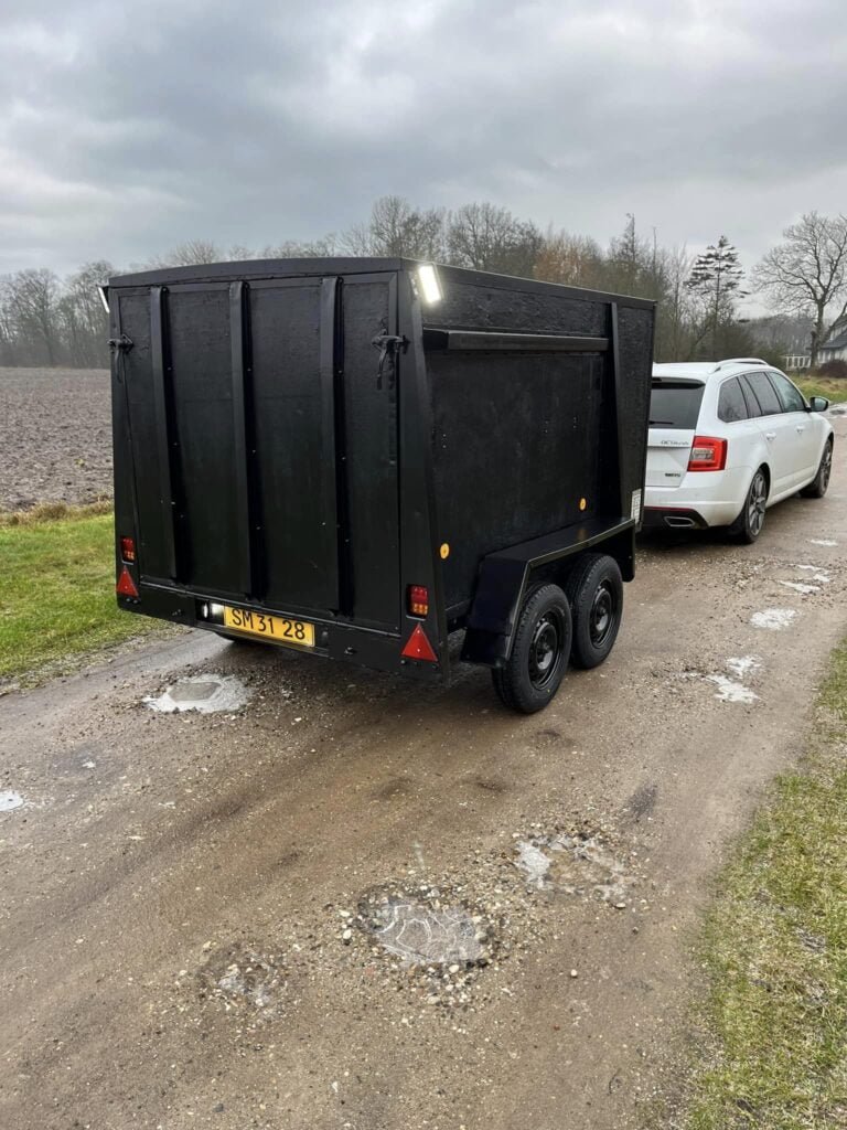 Hvid bil trækker sort trailer på grusvej