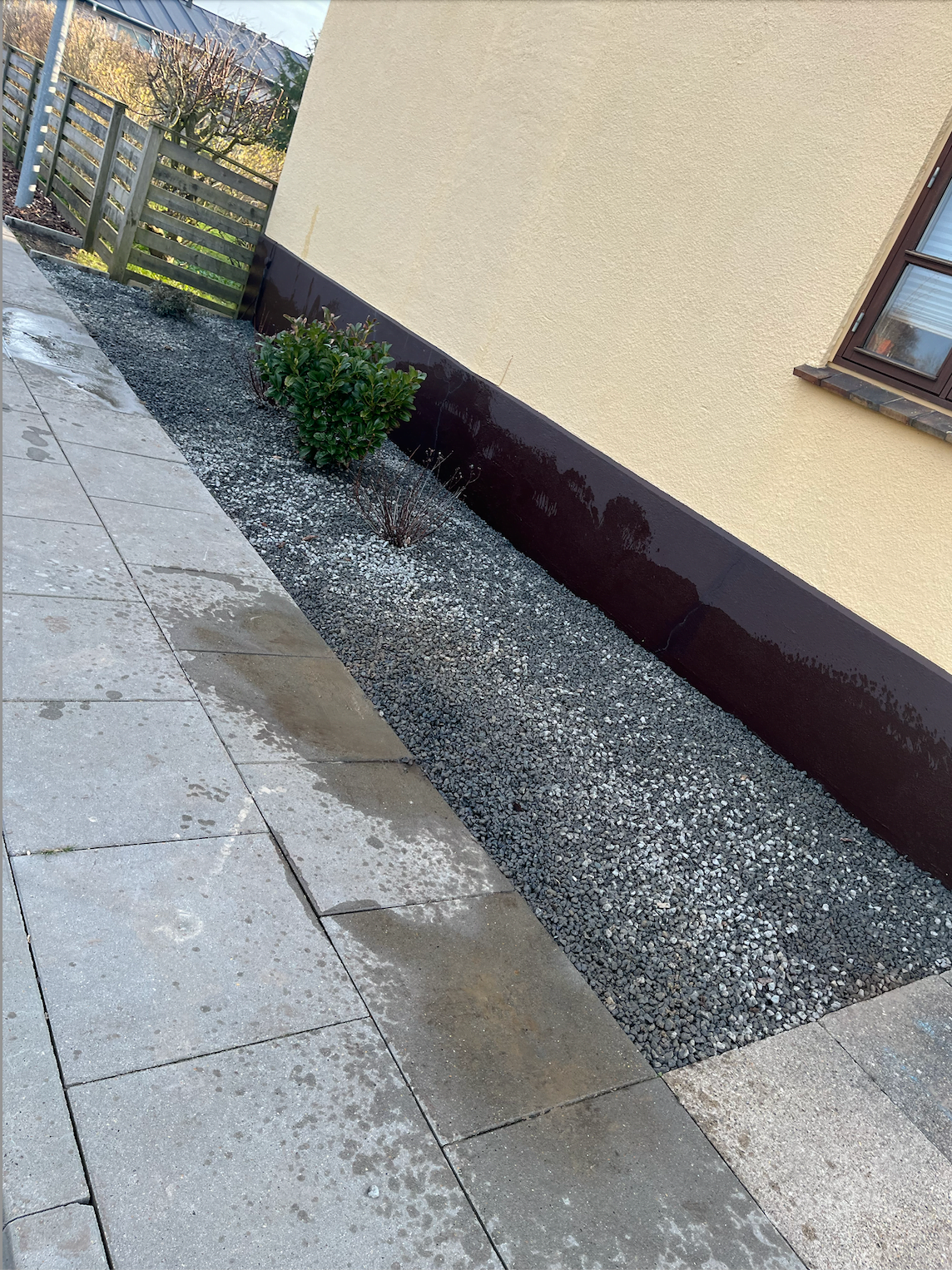 Stenbelagt havekant ved gul husmur